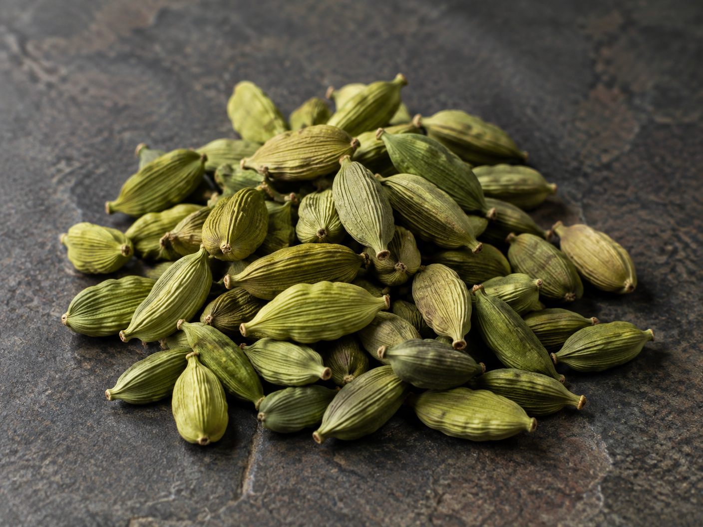 Natural green cardamom pods on a dark stone surface