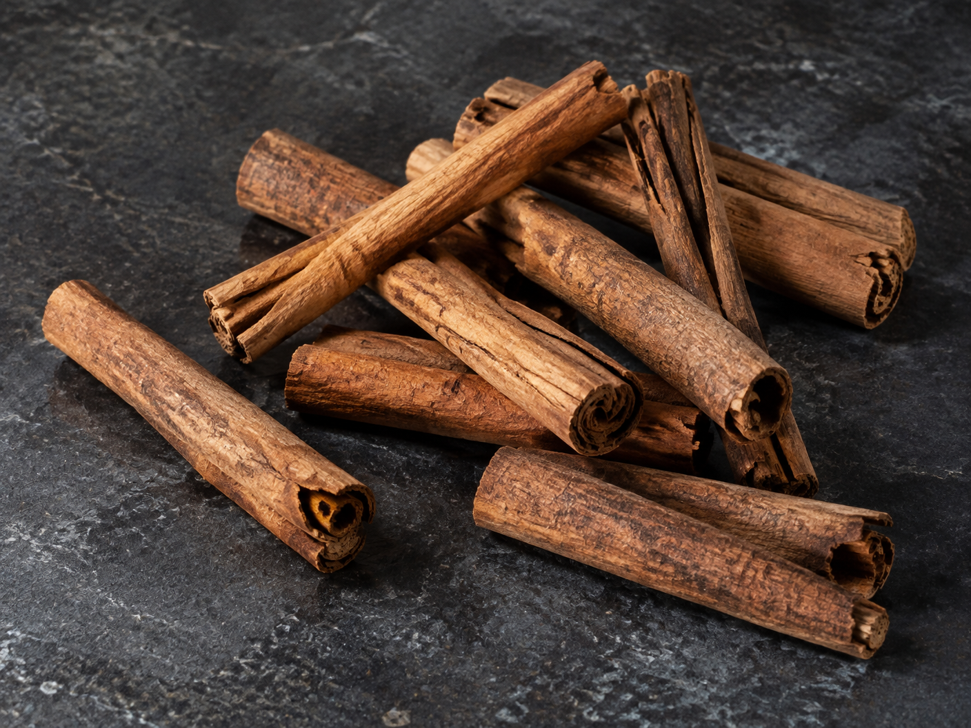 Natural dried cinnamon quills on a dark stone surface